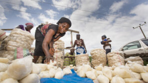 a Nigerian woman bends over bags of produce in a market