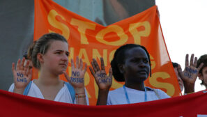 A white activist holds up her hands with "NO LNG", "NO FOSSILS" written on them, and a black activist's hands read "WE CAN'T DRINK OIL"